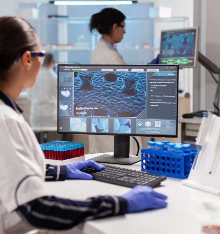 Biologist doctor checking DNA informations typing on pc in modern equipped laboratory. Scientists examining vaccine evolution in medical lab using high tech, chemistry tools for scientific research.